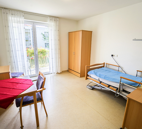 Helles Zimmer mit Pflegebett, Tisch und Stuhl