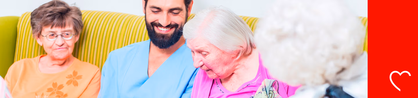 Pflegekraft sitzt mit mehreren Seniorinnen auf der Couch