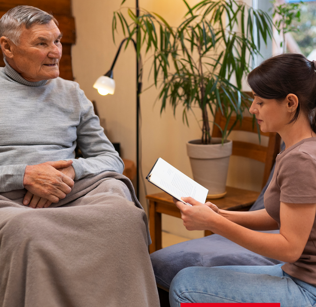 Mitarbeiterin liest einem älteren Mann etwas aus einem Buch vor