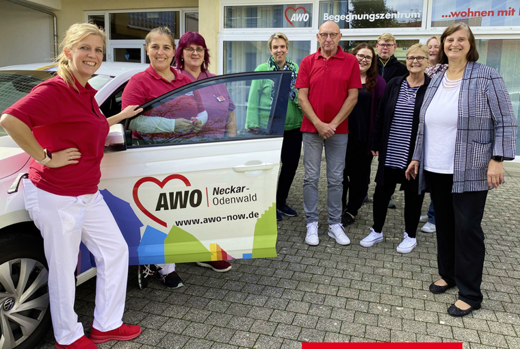 Gruppe von Menschen mit einem AWO-Fahrzeug auf Parkplatz